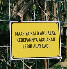 a yellow sign hanging from the side of a wire fence next to a green tree