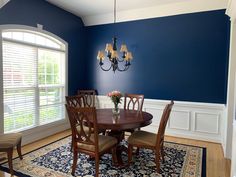 a dining room with blue walls and white trimmings on the ceiling, along with an area rug