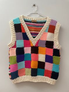 a multicolored knitted sweater vest hanging on a white hanger against a wall