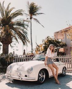 a woman sitting on the hood of a white car in front of a palm tree