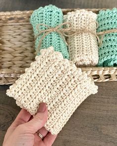 a hand is holding some crocheted items in front of a basket full of them