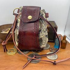 Looking for a stylish storage solution for your dice? Coin pouch for your Larp costume or D&D cosplay? This handcrafted leather bag might just be for you. Mahogany Brown hand stained vegtan leather main band with tan braided detail, and Golden metallic snake print soft leather circle body section.  Brass coloured metalwork including a press popper to the front, eyelets on all the drawstring holes, 2 D-rings, and a deaths head hawk moth charm. Size: approximately 130mm tall and wide Images show t Vintage Brown Bag For Personal Use, Handmade Brown Pouch Bucket Bag, Medieval Style Handmade Pouch For Everyday Use, Steampunk Leather Bag For Everyday Use, Vintage Handmade Brown Pouch, Handmade Brown Vintage Pouch, Medieval Handmade Pouch For Everyday Use, Vintage Handmade Leather Pouch, Handmade Vintage Leather Pouch