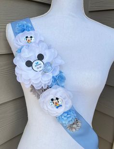 a white dress with blue flowers and mickey mouses on the front, along with a light blue ribbon