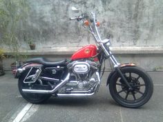 a red and black motorcycle parked in a parking lot next to a concrete wall with potted plants