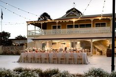 an outdoor dining area with tables and chairs in front of a large house at dusk