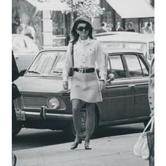 an old photo of a woman walking down the street in front of some parked cars