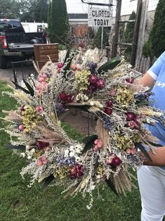 a woman standing next to a wreath with dried flowers on it in the middle of grass