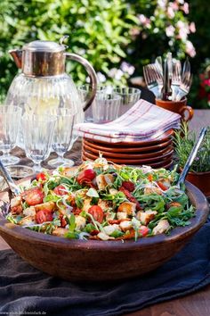 a wooden bowl filled with salad sitting on top of a table next to plates and silverware