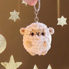 a crocheted sheep keychain hanging from a star - shaped background with gold stars