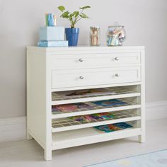 a white dresser with magazines and plants on top