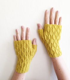 two hands wearing yellow knitted gloves against a white wall