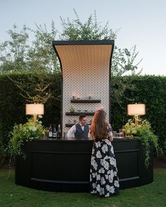 a woman standing in front of a bar with a man sitting at it's back