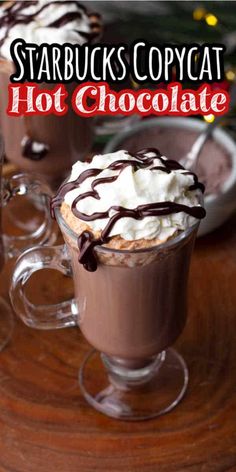 two cups filled with hot chocolate and whipped cream on top of a wooden table next to a christmas tree