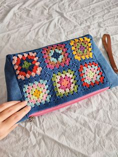 a hand is holding onto a crocheted blue purse on a white bed sheet