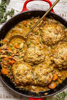 a pot filled with meatballs and vegetables on top of a wooden table next to a spoon