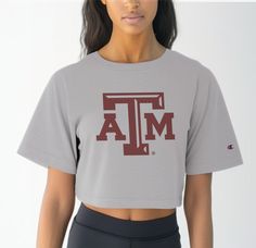 Elevate your Aggie game day attire with our Women's Texas A&M Logo Crop Top, a timeless piece that exudes pride and tradition. Crafted from premium 100% cotton, this tee ensures superior comfort during those intense moments cheering on the Aggies at Reed Arena or exploring the scenic beauty of Aggieland. Featuring the iconic Texas A&M logo front and center, this crop top is a true testament to your Aggie spirit. Whether you're attending class or hitting up Northgate for post-game celebrations, t Collegiate Athletic Heather Tops For Game Day, Game Day Tops In Athletic Heather, Game Day Pre-shrunk Athletic Heather Tops, Collegiate Style Tops In Athletic Heather For Game Day, Collegiate Athletic Heather Tops For Sports Events, Collegiate Athletic Heather Tops For Fan Gear, University Logo Short Sleeve Top For Sports Season, Collegiate Athletic Heather Tops With Letter Print, Athletic Heather Collegiate Top With Letter Print