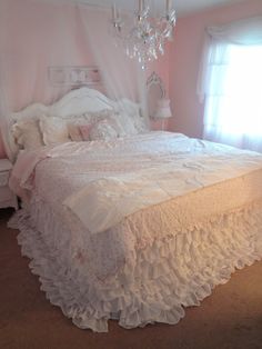 a white bed sitting in a bedroom next to a window and a chandelier