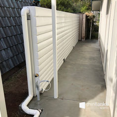 an outside view of a white fence with pipes running along it and a house in the background