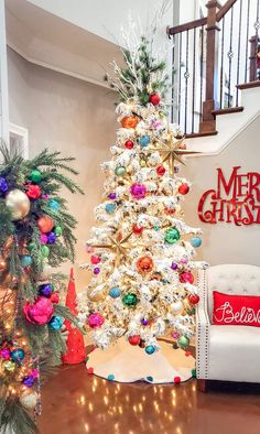 a decorated christmas tree sitting next to a white couch in front of a stair case