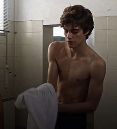 a shirtless man standing in a bathroom next to a sink and towel on a rack