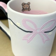 a white coffee cup with a pink bow on the side and a brown teddy bear