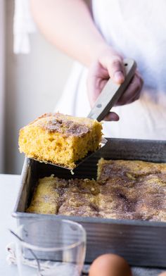 a person holding a knife cutting into a cake in a pan with other food on the table