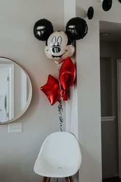 a mickey mouse balloon hanging on the wall next to a chair with balloons attached to it