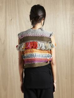 a woman standing in front of a wooden wall wearing a multicolored knitted vest