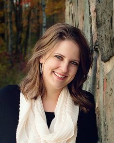 a woman wearing a white scarf leaning against a stone wall with trees in the background