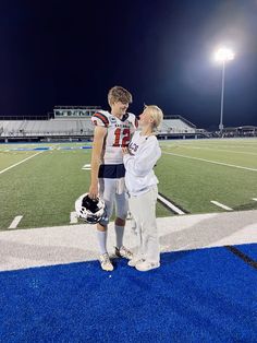 a man and woman standing on a football field at night with lights in the background