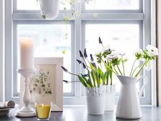 three white vases filled with flowers sitting on top of a window sill next to a candle