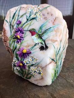 a rock with flowers and a hummingbird painted on it's side sitting on a table