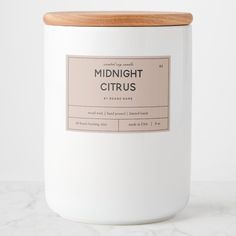 a white candle with a wooden lid sitting on a marble countertop next to a bottle of midnight citrus