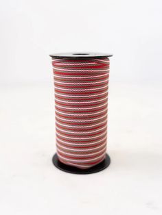 a spool of red and white striped ribbon on a black stand against a white background