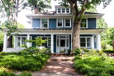 a blue house with white trim and trees in the front yard on a sunny day