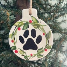 a ceramic ornament with a dog's paw and berries on it hanging from a christmas tree