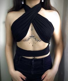 a woman with tattoos on her chest wearing black pants and a halter neck top