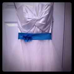 a white dress with a blue flower on the waist and belt is hanging in front of a door