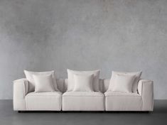 a white couch sitting in front of a wall with four pillows on top of it