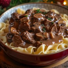 a red bowl filled with pasta and meat covered in gravy on top of a wooden table