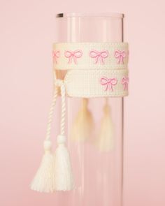 a pink ribbon with bows and tassels hanging from it's side in front of a glass vase