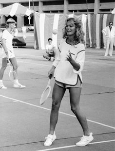 a woman holding a tennis racquet on top of a tennis court with other people in the background