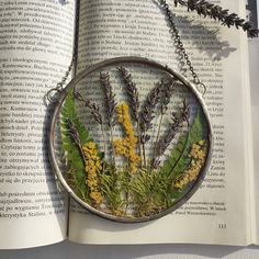 an open book with flowers and leaves on it, sitting next to a chain link necklace