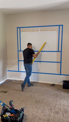 a man is painting the walls in his living room with blue tape and a yellow stick