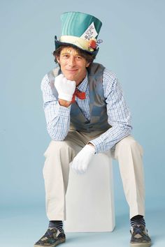 a man wearing a hat and gloves sitting on top of a white block with his hand under his chin