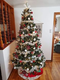 a decorated christmas tree in the corner of a living room with wooden floors and stairs