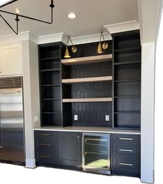 an empty kitchen with black cabinets and silver appliances in the center, along with gold pendant lights hanging from the ceiling