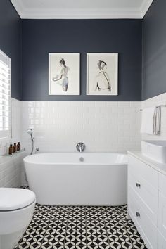 a white bath tub sitting next to a toilet under two pictures on the wall in a bathroom