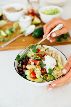 a person holding a fork in a bowl filled with vegetables, rice and black beans