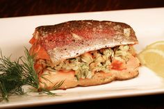 a piece of fish on a plate with lemon wedges